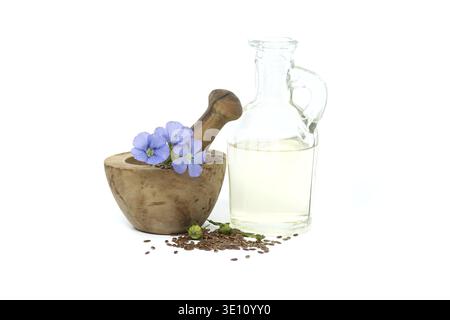Leuchtende blaue Flachsblume sitzt auf Holzmörtel, gefüllt mit kleinem braunem Leinsamen in der Nähe von Leinöl in Glasdekanter isoliert auf weißem Hintergrund Stockfoto