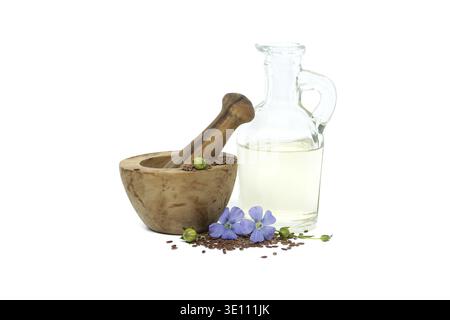 Leuchtende blaue Flachsblume sitzt auf Holzmörtel, gefüllt mit kleinem braunem Leinsamen in der Nähe von Leinöl in Glasdekanter isoliert auf weißem Hintergrund Stockfoto
