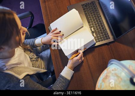Schüler lernen von zu Hause aus. Junge Frau, die online unterrichtet, Notizen macht, liest und lernt, während der Quarantäne am Schreibtisch zu Hause sitzen Stockfoto
