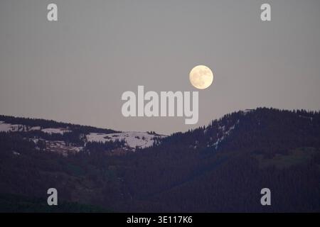 Der Vollmond zeigt sich in der Abenddämmerung mit schneebedeckten Bergen. Idaho, USA Stockfoto