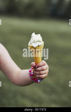 Nahaufnahme von childs Hand, die Kegel mit Eis über einen einfachen natürlichen, grünen Hintergrund. Ehrliche Menschen, echte Momente, in authentischen Situationen Stockfoto