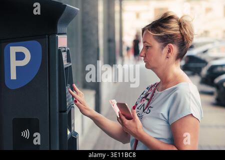 Frau Kauf einer Eintrittskarte für das Parken mit EC-Karte oder Handy, neben Parken der Maschine Stockfoto