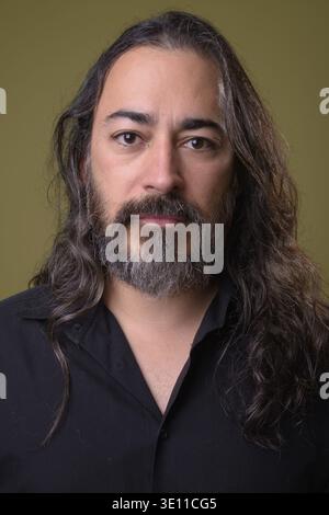 Studio-Aufnahme von reifem, gutaussehendem, bärtigen, multiethnischen Geschäftsmann mit langen Haaren vor farbigem Hintergrund Stockfoto