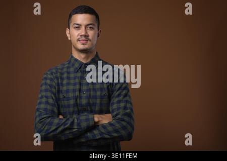 Studio shot Junger multi-ethnischen asiatischer Mann in Grün kariertem Hemd gegen braunen Hintergrund Stockfoto