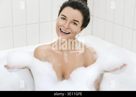 Glückliche junge Frau nimmt Bad mit einem Schaum Stockfoto