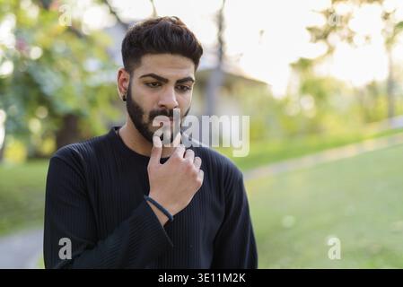 Junge schöne Indische Mann Denken mit der Hand am Kinn im Park Stockfoto