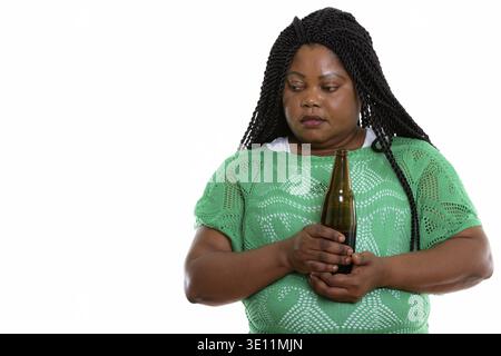 Studio-Schuss von fetter schwarzer Afrikanerin, die traurig aussieht, während sie denkt und eine Flasche Bier hält Stockfoto