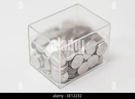 Transparente Kunststoffbox mit Münzen auf weißem Hintergrund. Konzept der Lagerung, Spende, Geldmultiplikation. Minimalistisches Image für Unternehmen p Stockfoto