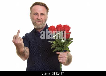 Studioaufnahme eines reifen bärtigen Mannes, der rote Rosen hält und dabei seinen Mittelfinger zeigt Stockfoto