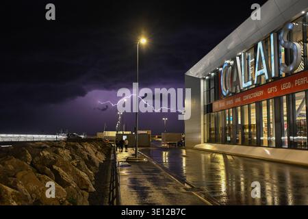 Ein kräftiger Blitz beleuchtet den Himmel über dem Hafen von Calais und dem Haupteinkaufskomplex der Fähre während eines schweren Gewitters im Frühling. Stockfoto