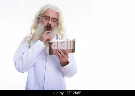 Studio shot der älteren bärtigen Mann Arzt zu denken, während mit digitalen Tablet Stockfoto