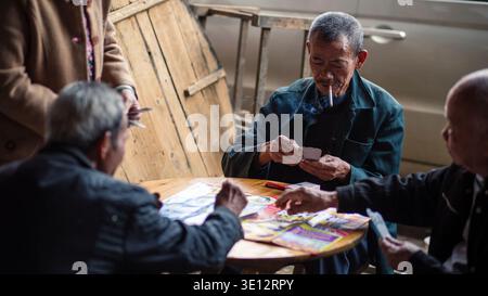 Ältere chinesische Männer spielen Karten und rauchen am runden Tisch im Dorf Longsheng, China Stockfoto