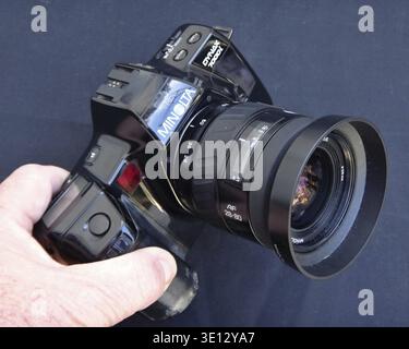 Die Hand hält eine schwarze Minolta Dynax 700si 35-mm-Filmkamera mit angesetztem 28-80-mm-Zoomobjektiv Stockfoto