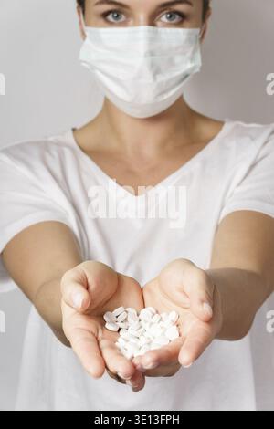 Eine junge Frau mit Gesichtsmaske hält eine weiße Pille Stockfoto