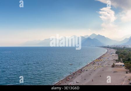 Luftpanorama des Konyaalti Beach in Antalya, Türkei, mit Liegestühlen am Ufer und Taurusgebirge, die in den trüben Horizont eintauchen. Stockfoto