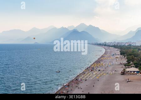 Panoramablick auf Konyaalti Beach, Antalya, mit Taurusgebirge, Parasailing, Sonnenliegen, und Mittelmeer. Stockfoto