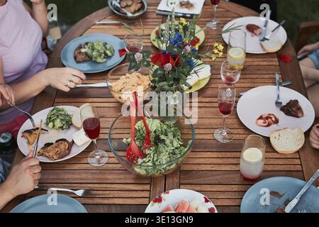Familie mit einer Mahlzeit vom Grill während des Sommer Picknick im Freien Abendessen in einem Hausgarten. Nahaufnahme von Leuten, die an einem Tisch mit Essen und Geschirr sitzen Stockfoto
