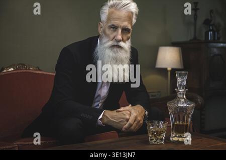 Stilvoller und schöner bärtiger älterer Mann, der Whisky trinkt Stockfoto