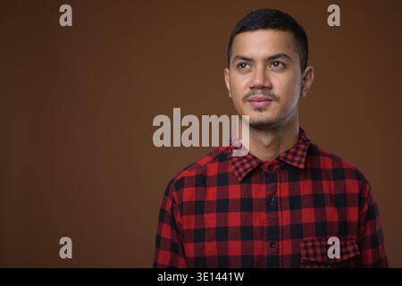 Studio shot Junger multi-ethnischen asiatischer Mann tragen rot kariertem Hemd gegen braunen Hintergrund Stockfoto