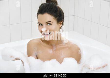 Glückliche junge Frau nimmt Bad mit einem Schaum Stockfoto