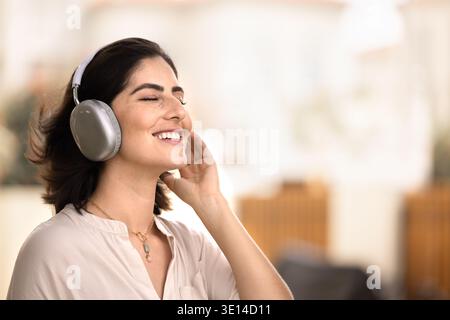 Glückliche, ruhige, junge Lateinfrau mit großen Kopfhörern Stockfoto