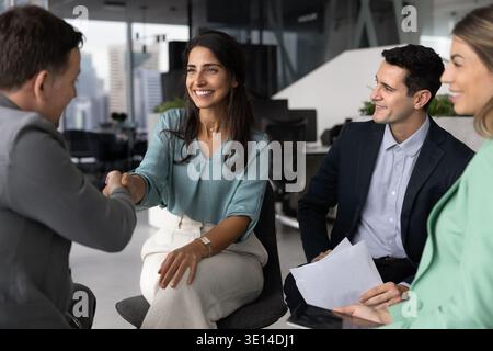 Lächelnde junge Geschäftsfrau, die im Team arbeitet und der Führungskraft die Hand schüttelt Stockfoto