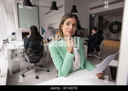 Hispanische Geschäftsfrau denkt an Papierdokumente mit Laptop am Schreibtisch Stockfoto