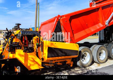 Das Baupersonal verwendet eine Pflastermaschine, da der Lkw Asphaltmischungen für Straßenreparaturen liefert Stockfoto