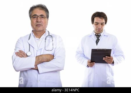Studio shot der Persischen mann Arzt mit verschränkten Armen und Jungen persischen Mann Doktor Lesung über Zwischenablage Stockfoto