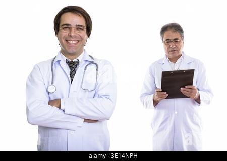 Junge glücklich Persischen mann Arzt lächelnd mit verschränkten Armen und Senior persischen Mann Doktor Lesung über Zwischenablage Stockfoto