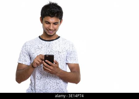 Studio shot junger indischer Mann glücklich lächelnd, während mit Handy Stockfoto
