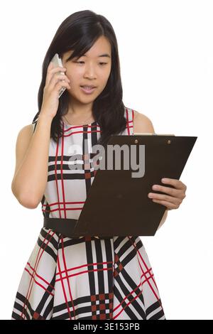 Junge schöne asiatische Geschäftsfrau lesen Zwischenablage beim Gespräch am Handy Stockfoto