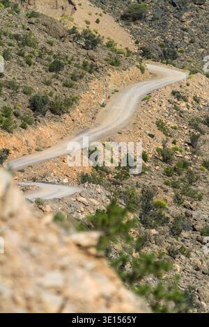 Gewundene Bergstraße, die durch einen steilen Canyon in den Al Hajar Mountains von Oman gehauen wurde. Stockfoto