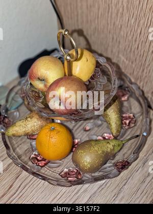 Frisches Obst Auf Glasständer, Äpfel Und Birnen Mit Orangen Und Verstreuten Granatapfelarten, Tiered Teller Auf Hölzerner Arbeitsplatte In Der Nähe Von Textu Stockfoto