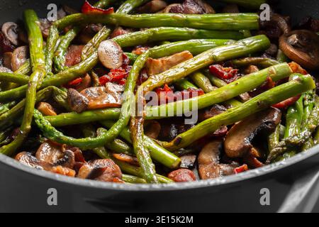Spargel, Speck und Pilzscheiben in einer Keramikpfanne im Hintergrund gebraten. Saisonales Gemüsekonzept kochen Stockfoto