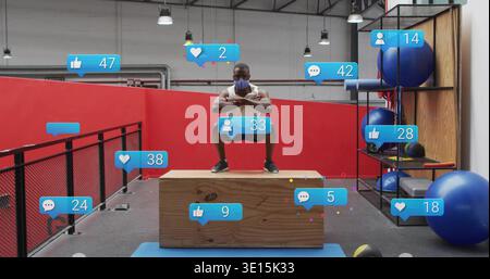 Hocker-Mann mit weißem ärmellosem Oberteil und Stoffmaske auf Plyometriekasten im Fitnessstudio, Social Overlays Stockfoto