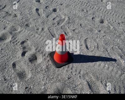 Isolierter orangefarbener Verkehrskegel auf Strandsand mit Fußspuren und Reifenspuren Stockfoto