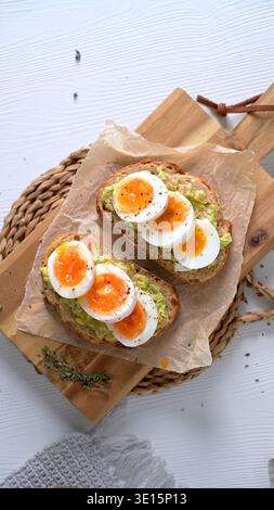 Zwei knusprige Brotscheiben mit cremiger Avocado und lebendig weich gekochten Eiern auf Pergamentpapier. Aufnahmen aus einem hohen Winkel mit hellem, natürlichem Licht Stockfoto