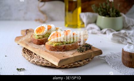 Zwei Scheiben knuspriger Sauerteig, belegt mit Avocadopüree und marmelierten weichen gekochten Eiern. Die sanfte natürliche Seitenbeleuchtung betont die cremige Textur des Stockfoto