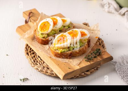 Zwei Scheiben gerösteter Sauerteig, belegt mit Avocadopüree und marmelierten weichen gekochten Eiern. Hoher Blickwinkel mit natürlichem hellem Licht und rustikalem Holz Stockfoto