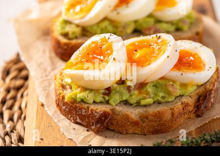 Knuspriger Sauerteig mit cremigem Avocado-Püree und perfekt marmelierten, weichen gekochten Eiern. Die Nahaufnahme hebt die leuchtenden orangefarbenen Eigelbe und das Meer hervor Stockfoto
