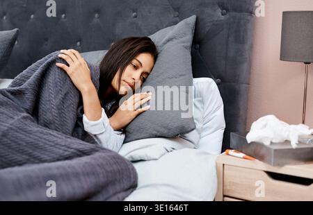 Krank, Frau und liegend mit Gewebe im Bett für Grippe, Virus oder Erkältung und Grippe zu Hause. Weibliche Person, Toilettenpapier oder Kissen mit Thermometer, Allergie Stockfoto