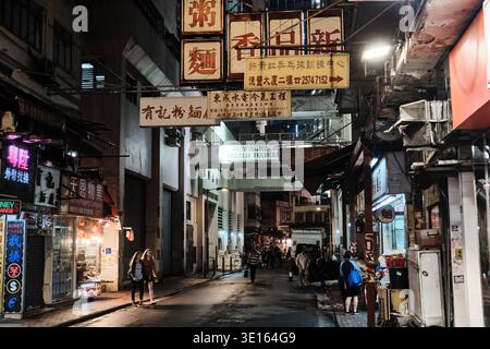 Neonbeleuchtete Gasse bei Nacht mit chinesischen Ladenschildern und Fußgängern in Hongkong, China. Stockfoto