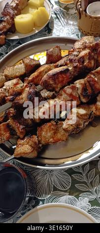 Gegrillte Fleischspieße auf einem Teller mit Kartoffeln und Geschirr auf einem Tisch. Köstliches Abendessen, gegrilltes Fleisch, Shish Kebab Stockfoto