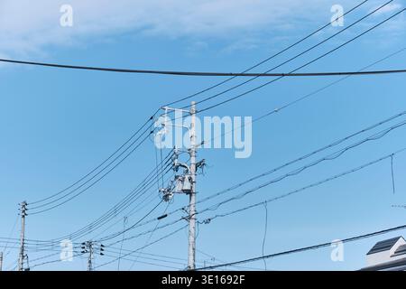 Stromleitungen und Strommasten vor einem klaren blauen Vorstadthimmel. Stockfoto