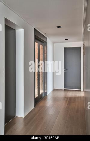 Minimaler Apartmentflur mit hellen Wänden, Holzboden und einfachen Türen. Stockfoto