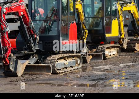 Minibagger auf nassem Baustellengelände mit Pfützen, die Baumaschinenflotten, Baustellenbetrieb und Mietlogistik repräsentieren Stockfoto