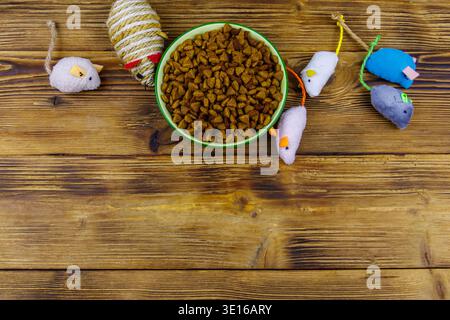 Set von Maus Spielzeug für Katze und Schüssel mit trockenem Tierfutter auf hölzernem Hintergrund. Draufsicht, Kopierraum. Haustierpflegekonzept Stockfoto
