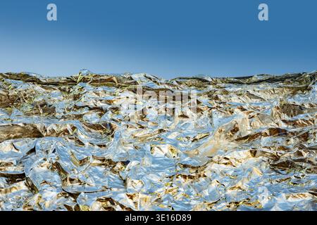 Zerknitterte silberne Aluminiumfolie schafft eine abstrakte Metallic-Landschaft unter blauem Himmel Stockfoto