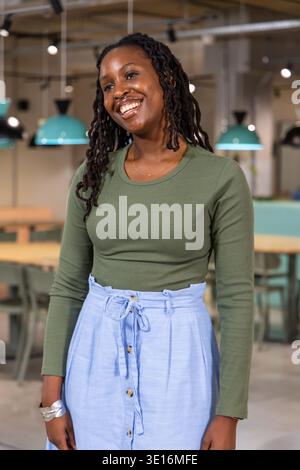 Afroamerikanerin steht mit olivfarbenem blauem Rock goldener Halskette in Café-Teal-Lampen Stockfoto